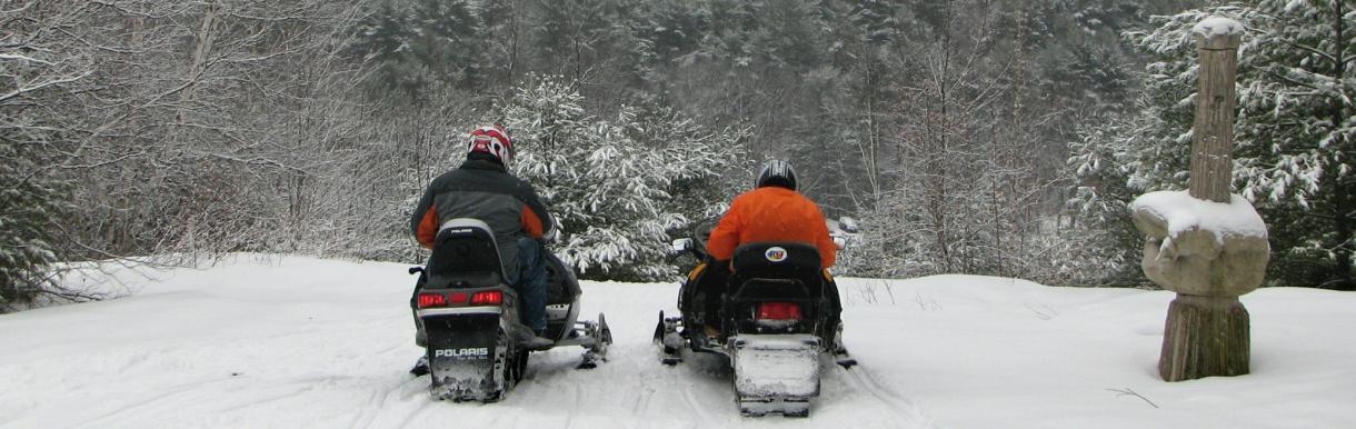 Rear view of 2 snowmobilers in full winter gear at andres overlooking town library