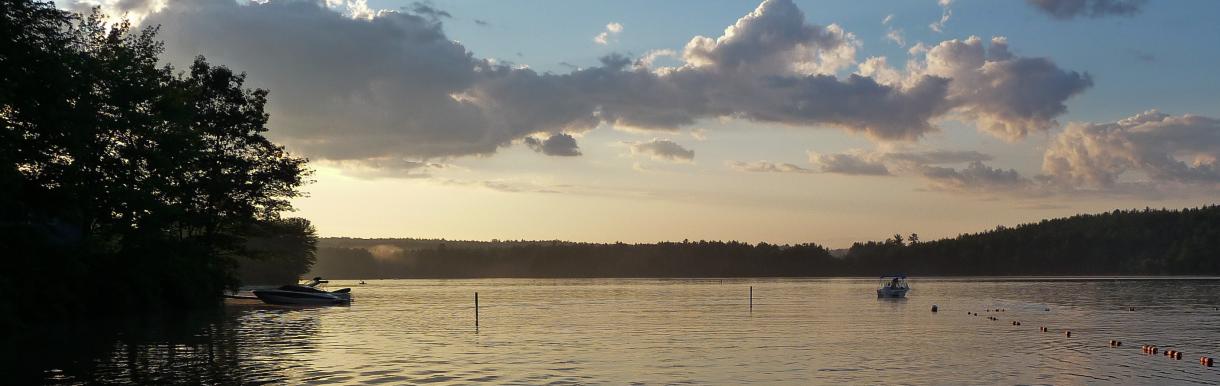 Clouds at dusk over calm water - few boats in water, trees along short at left